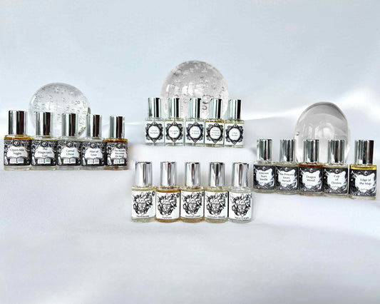 All Twenty A House on the Moon 5mL glass perfume bottles with silver tops grouped by collection on a white cloth with clear spheres behind.