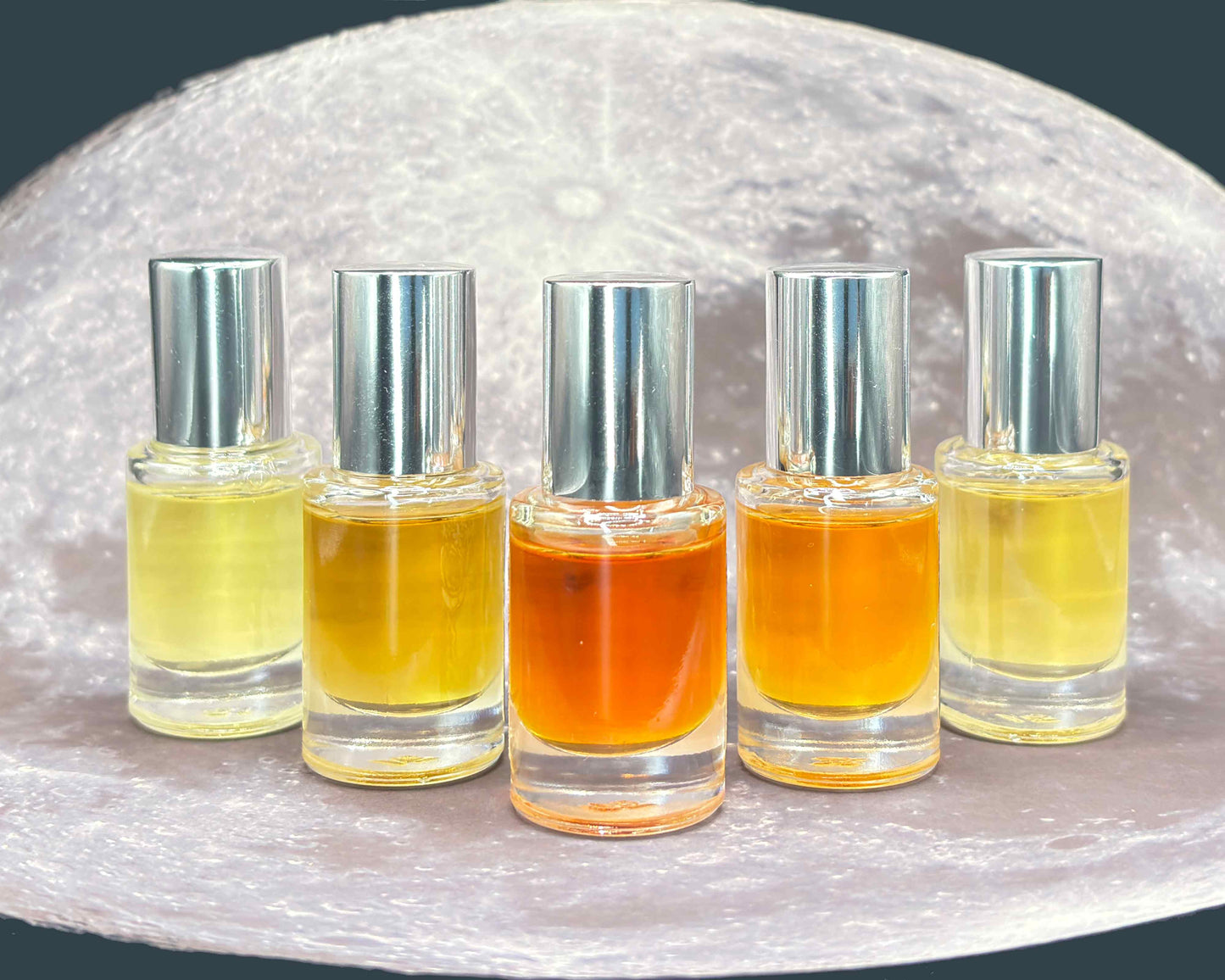 Five glass 5 mL bottles with varying colored perfume lined up on a moonscape.