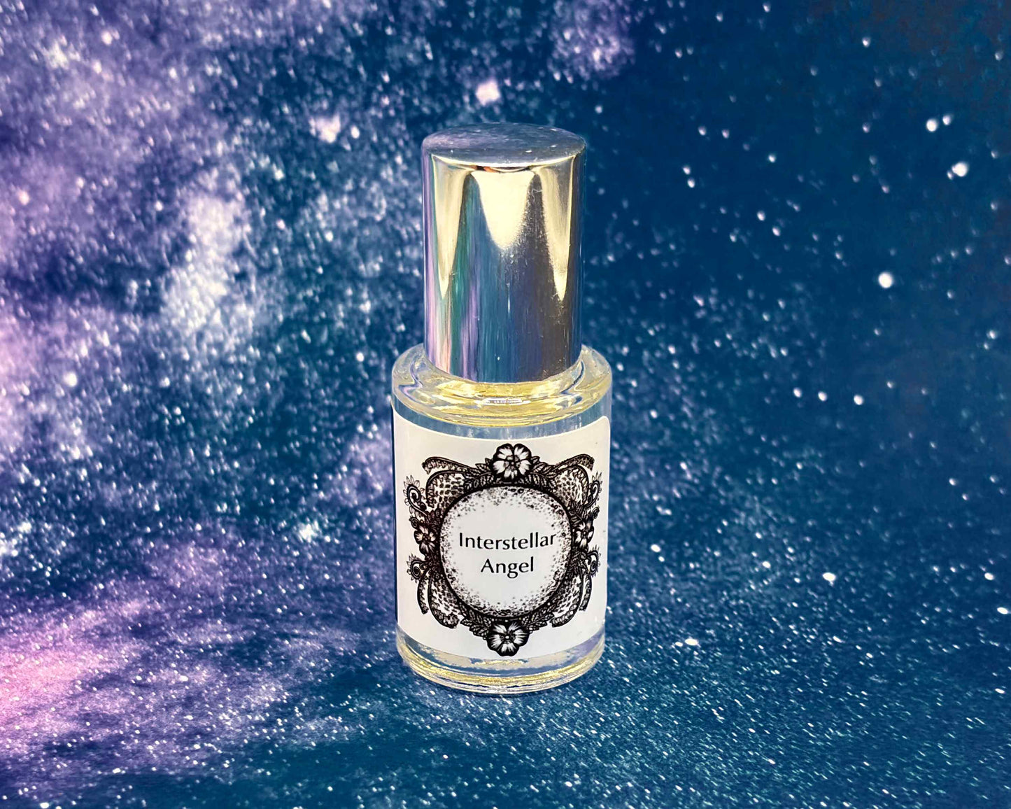 5 mL glass perfume bottle with silver cap of the scent "Interstellar Angel" in front of a blue galaxy background.
