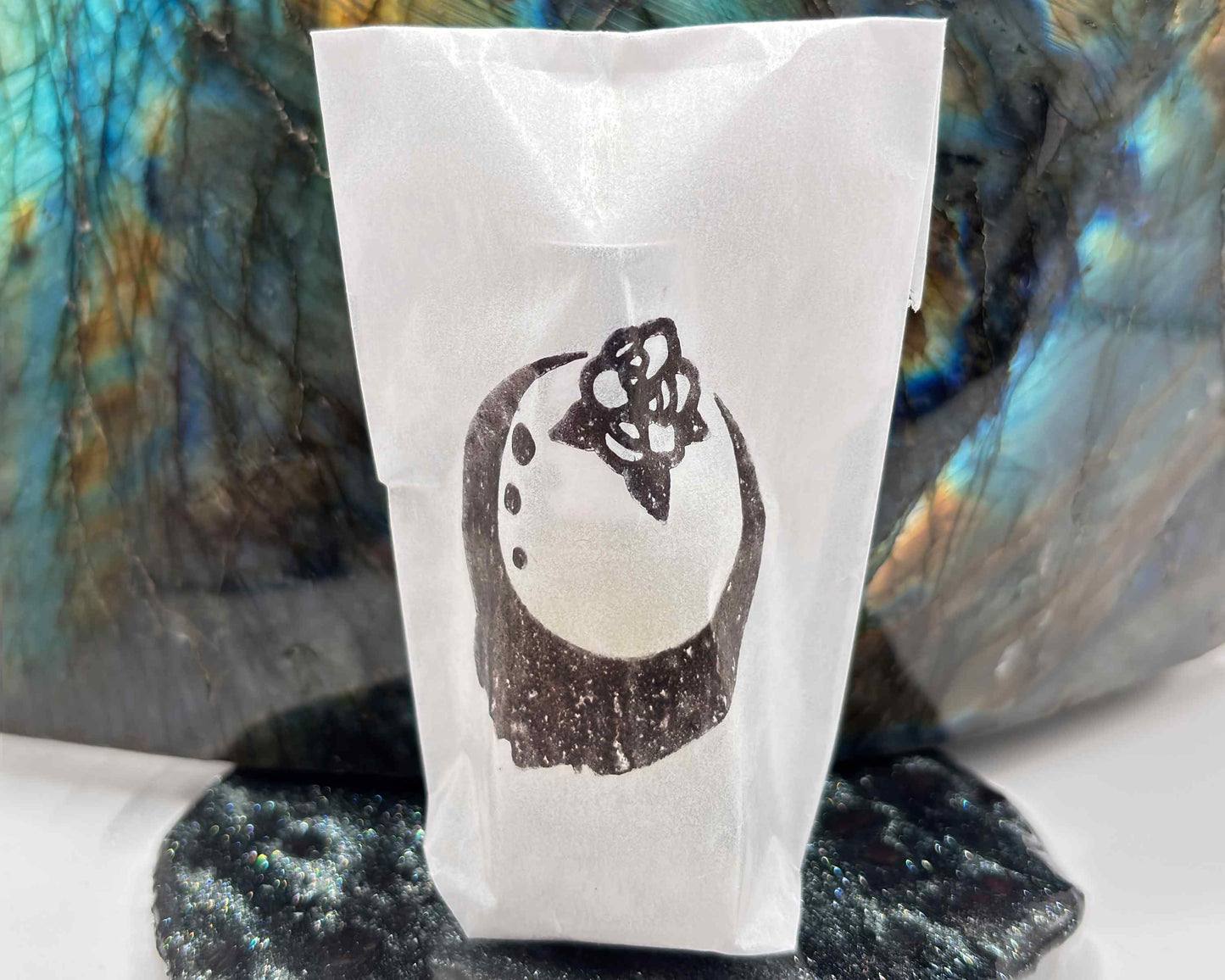 Close-up view of perfume bottle packaged in a glassine envelope, in front of a labradorite crystal.