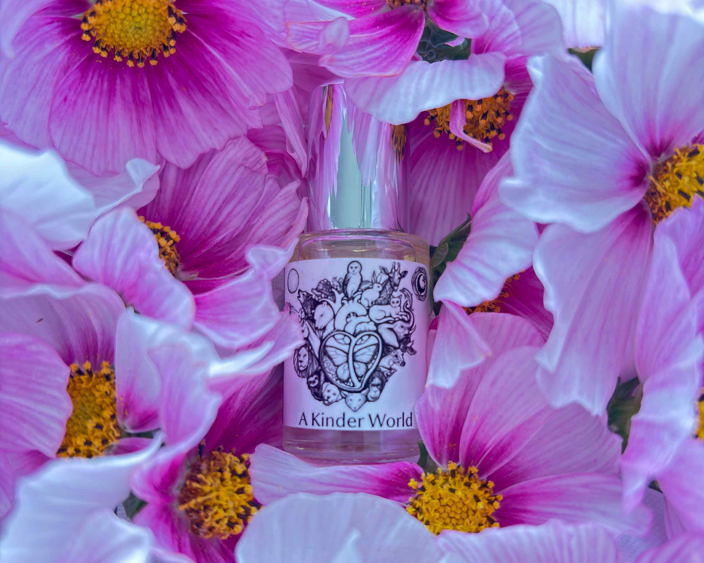 5 mL glass perfume bottle with silver cap of the scent "A Kinder World" nestled in a bed of pink cosmos flowers.
