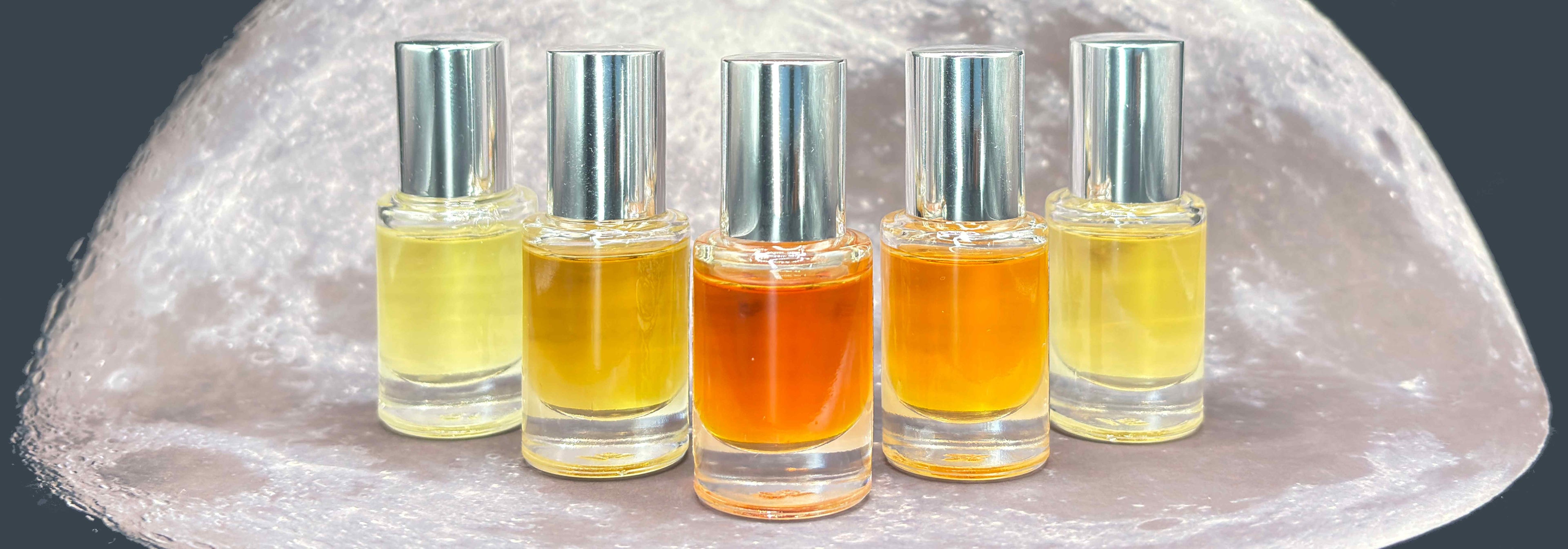 Five glass 5 mL bottles with varying colored perfume lined up on a moonscape.