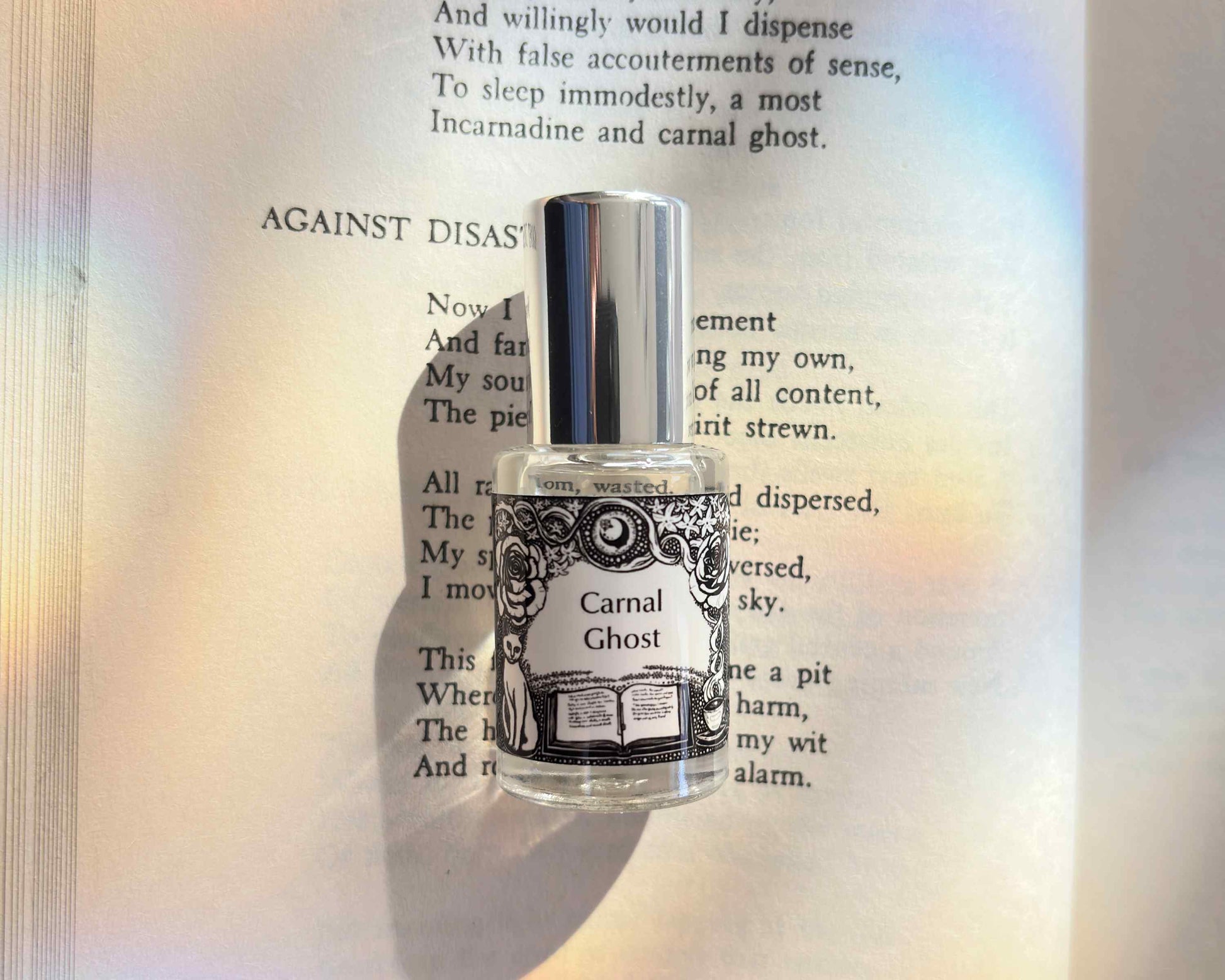 5 mL glass perfume bottle with silver cap of the scent "Carnal Ghost" laid atop a book open to the poem it was inspired by.