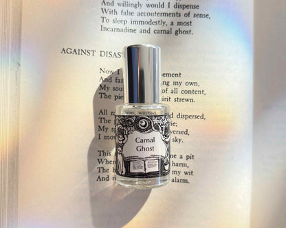 5 mL glass perfume bottle with silver cap of the scent "Carnal Ghost" laid atop a book open to the poem it was inspired by.