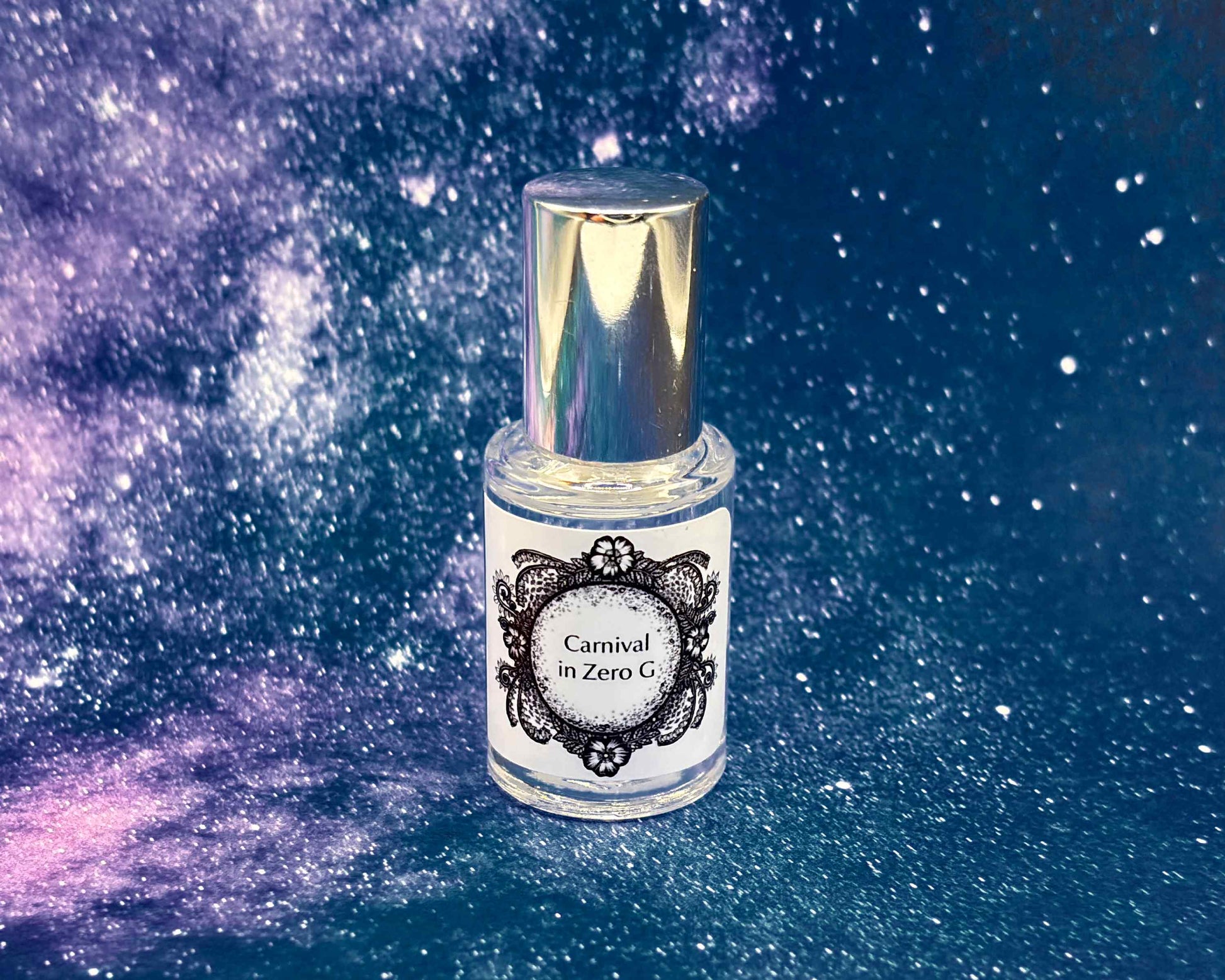 5 mL glass perfume bottle with silver cap of the scent "Carnival in Zero G" in front of a blue galaxy background.