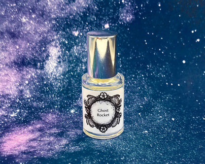 5 mL glass perfume bottle with silver cap of the scent "Ghost Rocket" in front of a blue galaxy background.