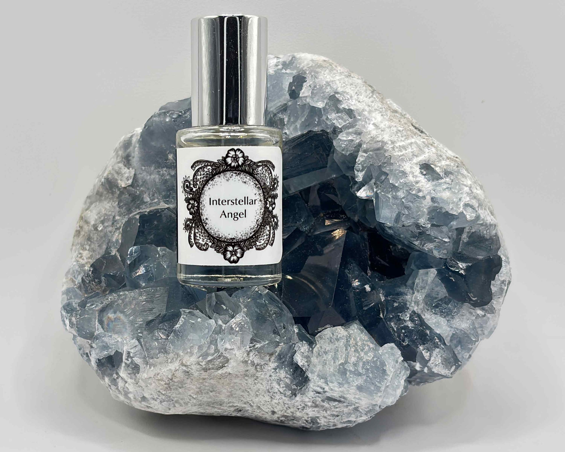 5 mL glass perfume bottle with silver cap of the scent "Interstellar Angel" nestled in a blue celestite crystal.