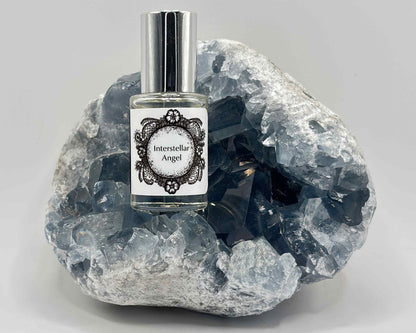 5 mL glass perfume bottle with silver cap of the scent "Interstellar Angel" nestled in a blue celestite crystal.