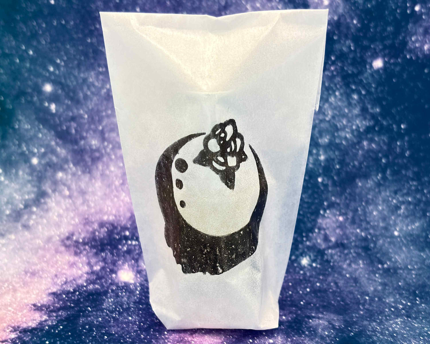 Close-up view of perfume bottle packaged in a glassine envelope, in front of a blue galaxy.