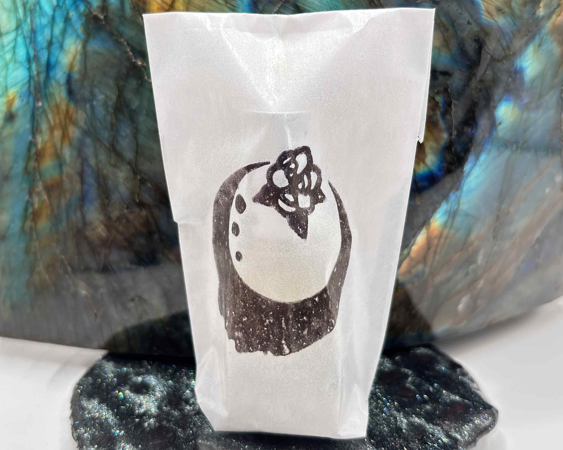 Close-up view of perfume bottle packaged in a glassine envelope, in front of a labradorite crystal.