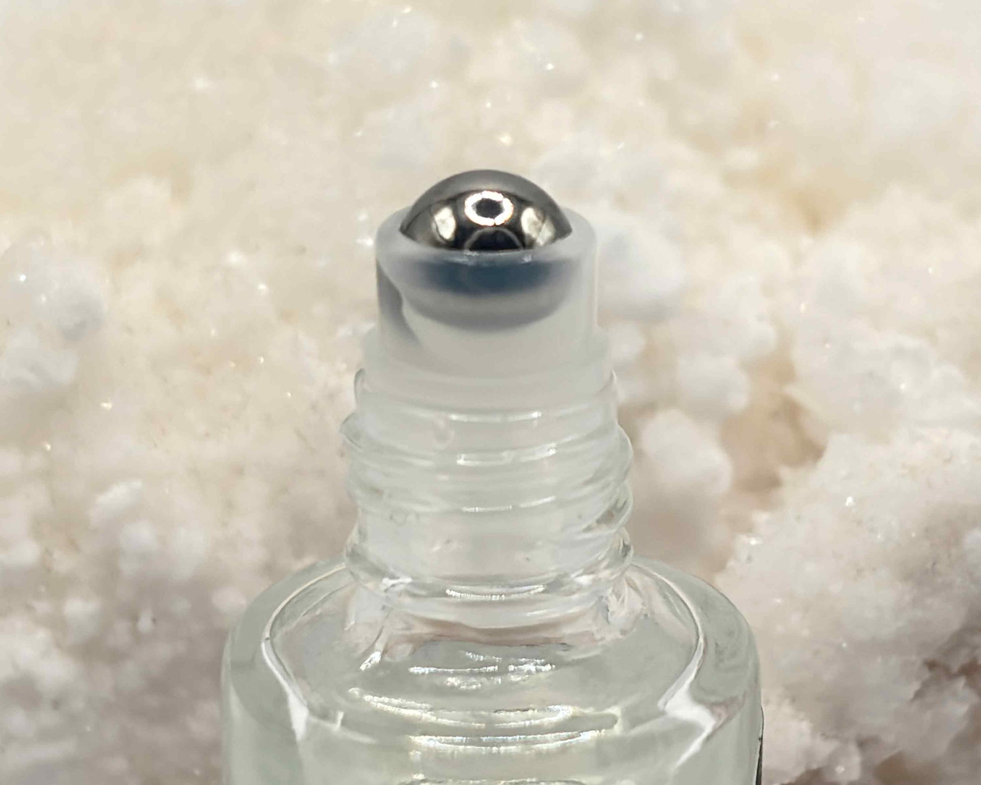 Close-up view of perfume bottle roller top, in front of an aragonite crystal.