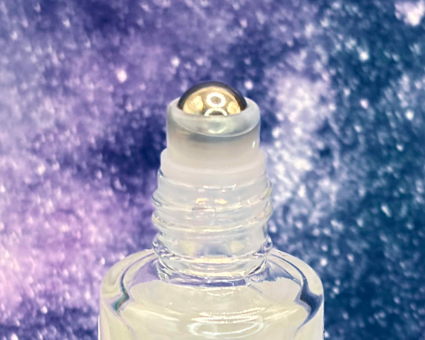 Close-up view of perfume bottle roller top, in front of a blue galaxy.