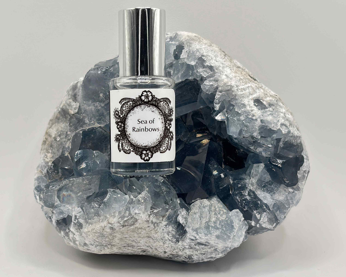 5 mL glass perfume bottle with silver cap of the scent "Sea of Rainbows" nestled in a blue celestite crystal.