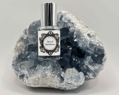 5 mL glass perfume bottle with silver cap of the scent "Sea of Rainbows" nestled in a blue celestite crystal.